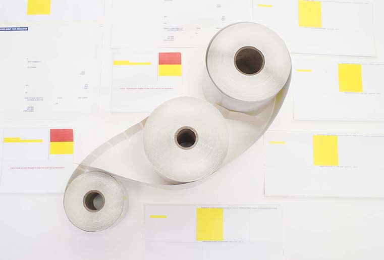 A roll of pharmacy labels sitting atop a variety of multicolored sheets of stationery.