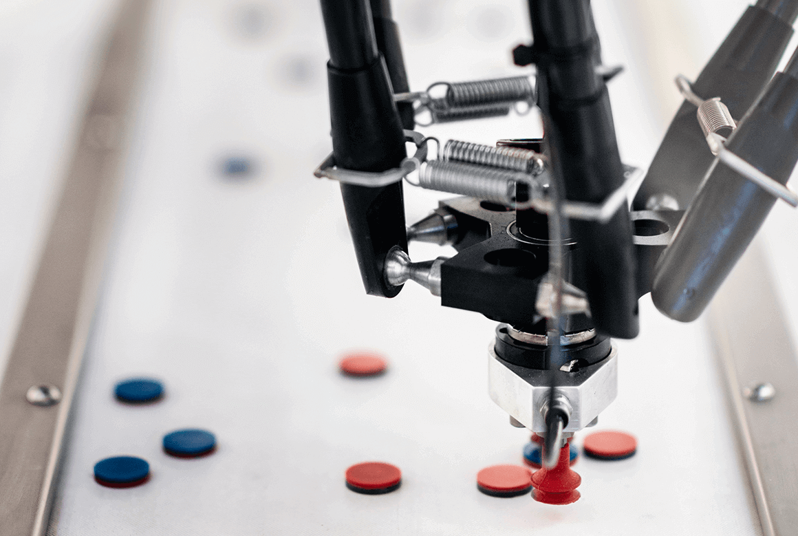 A robotic component presses a plastic disk on a convey or belt, showcasing pharmacy automation systems.